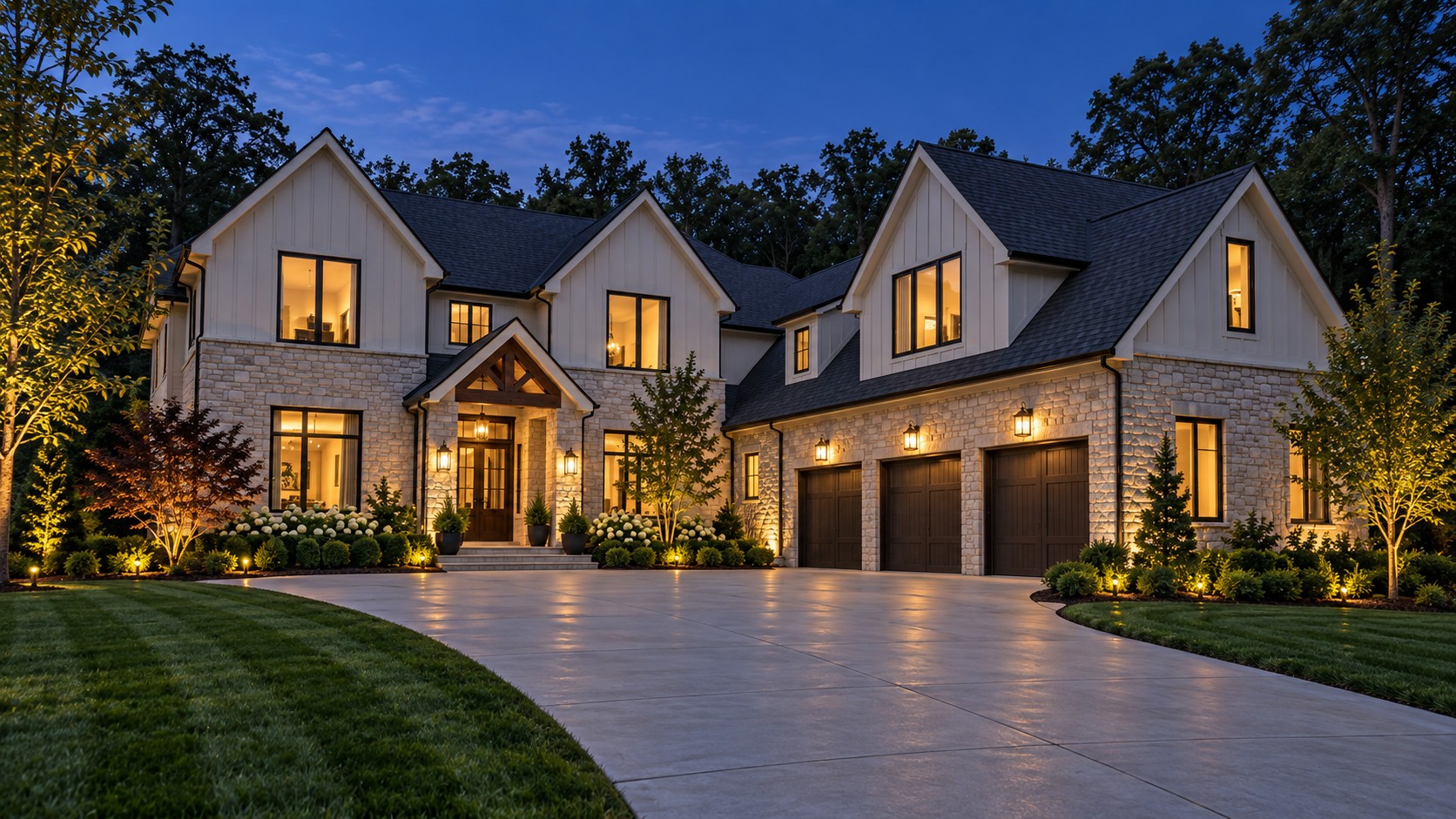 Broom-finish concrete driveway sweeping to a stone and siding home at blue hour, lanterns lit
